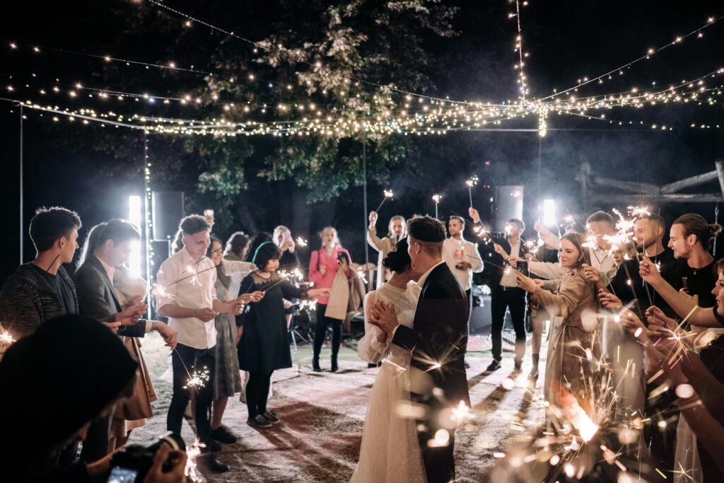 pexels-photo-15964966-15964966 A couple dances under twinkling lights at a wedding reception, surrounded by guests holding sparklers.